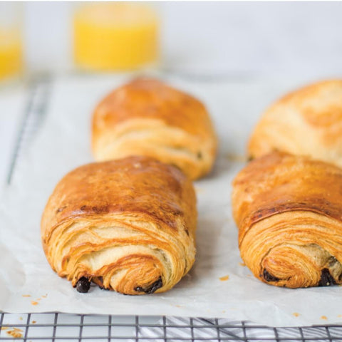4 Chocolate croissants placed on baking paper on a grid, front view. 