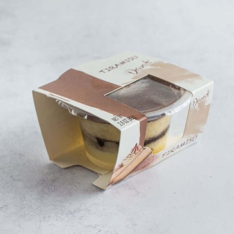 Tiramisu Dessert Cups in its cardboard packaging, placed on marble, side view.