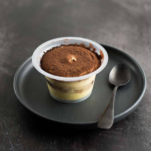 Tiramisu Dessert Cups opened and placed on round plate with a spoon, front view.