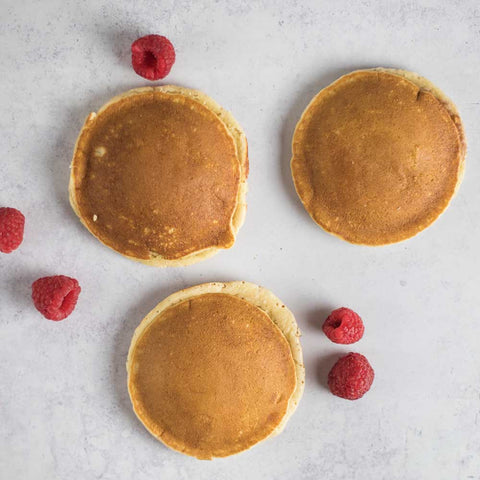 3 Strawberry-Filled Pancake placed on a marble with some raspberries next to it, seen from above.