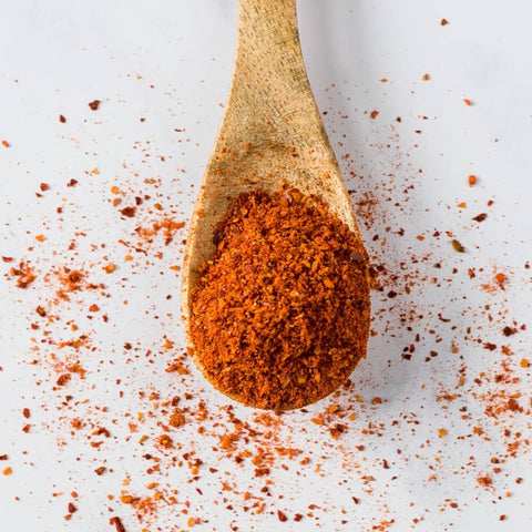 Wooden spoon containing Espelette Chili Pepper PDO spices, seen from above.