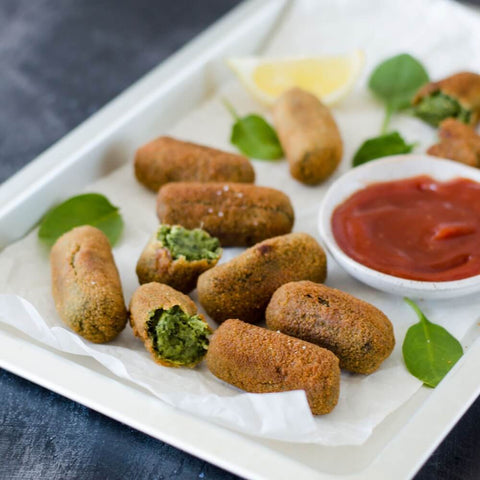 Spinach and Pine Nuts Croquettes cooked and arranged in a tray with salad leaves and sauce, front view.