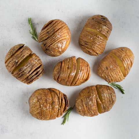 Hasselback Potatoes cooked and sliced, arranged on marble with thyme, seen from above. 
