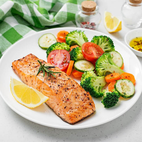 Cooked Norwegian Salmon arranged on a round plate with tomatoes, broccoli and lemon, front view.
