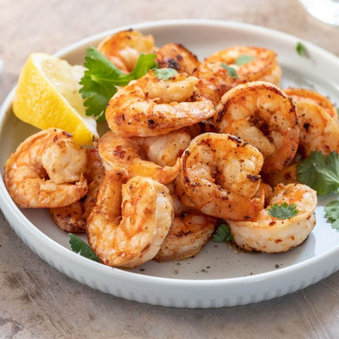 Assortment of Ez-Peel Shrimp cooked and arranged in a round plate with some basil leaves and lemon, seen from above.