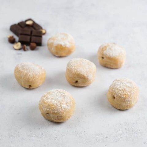 Assortment of 6 Mini Beignets Chocolate and Hazelnut arranged on marble, front view.
