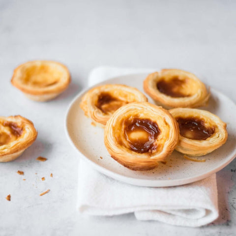 Assortment of 4 Past??is de Nata arranged in a round plate on marble, front view.