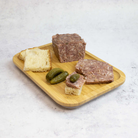 Hunter Venison an Pork Pate w/ Cranberries (Hunter Pate) arranged on a wooden board with two pieces of bread and 3 pickles, side view.