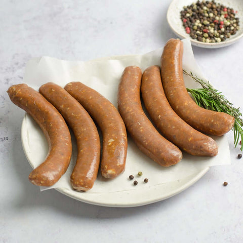 Lamb Merguez Sausage laid out in a round plate, on baking paper, with a branch of thyme and some black peppercorns, seen from above.