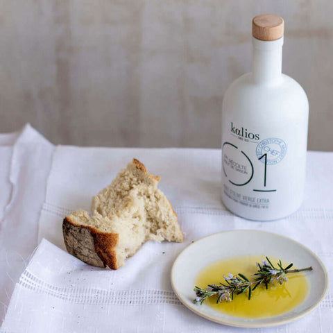 Bottle of Extra Virgin Olive Oil 01 from the Kalios brand, placed on a table with bread and a bowl filled with olive oil, front view. 