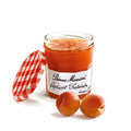 Glass jar of Apricot Preserve open from the Bonne Maman brand, with two apricot next to it, seen from the front.