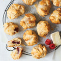 Assortment of 12 Raspberry & Brie Fillo Puffs arranged on a tray, with a piece of cheese and some raspberries, seen from above. 