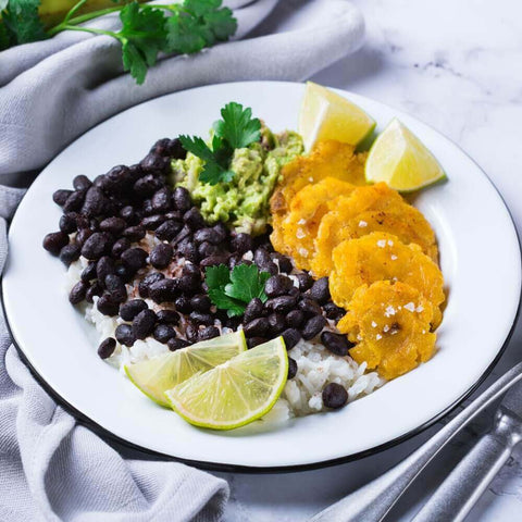 Crispy Pre-Fried Tostones cooked in a round plate with black beans, rice and lime, front view.