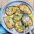 Assorted cooked and sliced eggplant, arranged on a round plate with some herbs, seen from above. 
