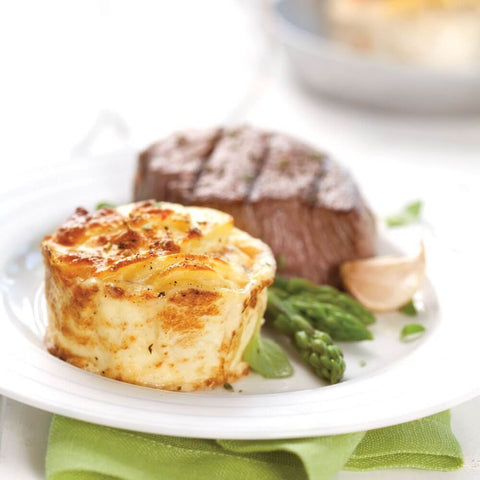 A Frozen Potatoes au Gratin in a round plate with a piece of red meat and some vegetables, placed on marble, seen from the front. 