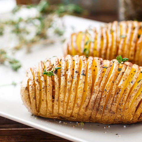 Hasselback Potatoes cooked and sliced, arranged on a board with thyme, front view.