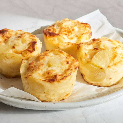 Assortments of 4 Frozen Potatoes au Gratin arranged on a round plate with a sheet of baking paper and placed on marble, front view. 