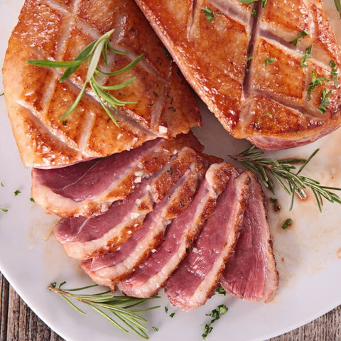 Cooked and sliced Moulard Magret Duck Breast, placed in a round dish, with a few branches of thyme, seen from above. 