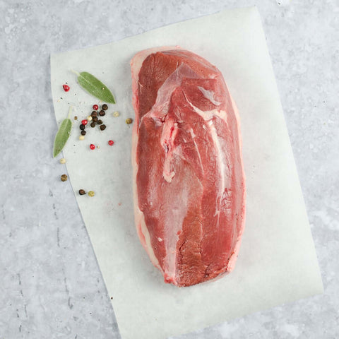Moulard Magret Duck Breast placed on a sheet of baking paper, on marble with some pink and black peppercorns, seen from above. 