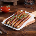 Chipolata Bistro Sausage cooked and placed on a sheet of baking paper on a wooden board, with a jar of sauce next to it, seen from the front.