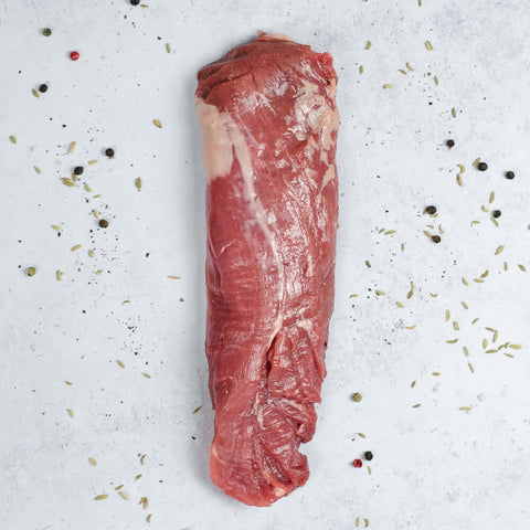 Iberico Pork Tenderloin arranged on marble with some black peppercorns, seen from above.