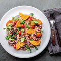 Small Octopus Tentacles Cooked with oranges, salad and tomatoes, arranged in a round plate, seen from above. 