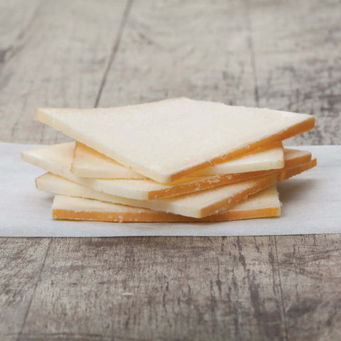 5 slices of raclette cheese stacked on baking paper, placed on a table, front view.