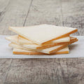 5 slices of raclette cheese stacked on baking paper, placed on a table, front view.