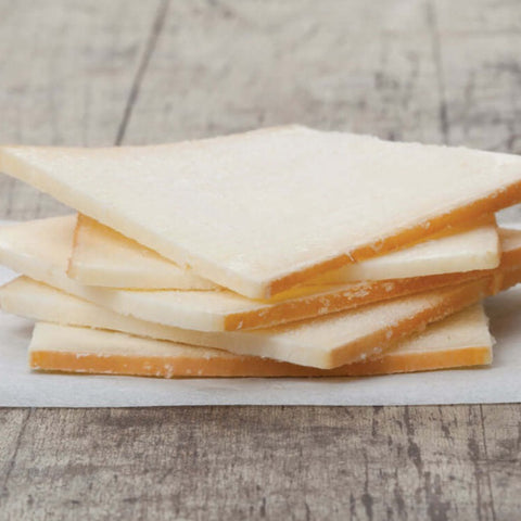 5 slices of raclette cheese stacked on baking paper, placed on a table, front view.