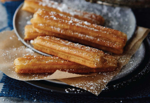 Assorted Caramel-Filled Churros baked and arranged in a round plate on a napkin, with powdered sugar sprinkled on top, seen from the front.