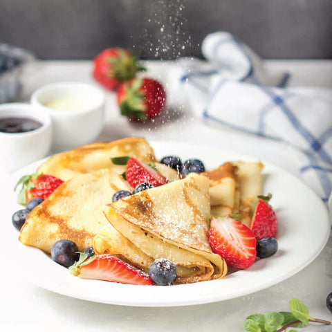 French Crepes placed in a round plate with some strawberries and blueberries, front view.