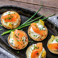 Assortment of 5 Mini Blinis cooked with smoked salmon and chives on top, arranged in a dish, seen from above.