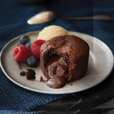 An open Lava Cake arranged on a plate with a scoop of vanilla ice cream, raspberries and blueberries on the side, seen from the front.