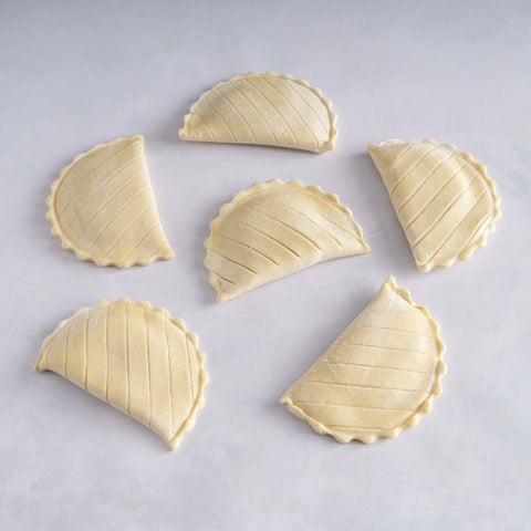 Assortment of 6 apple turnovers not yet baked, placed on marble, seen from above. 