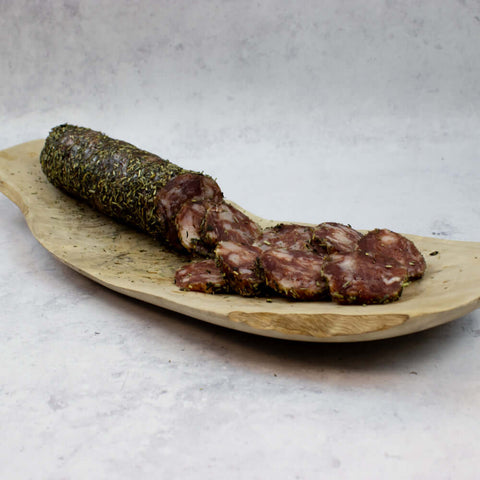French Pork Salami with Herbs sliced halfway through and placed on a wooden board, seen from the front.