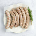 6 Chipolata Bistro Sausage laid out in a round plate, on baking paper, with a branch of thyme, seen from above.