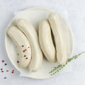 White Pudding Sausage (Boudin Blanc) laid out in a round plate, on baking paper, with a branch of thyme and some pink peppercorns, seen from above.