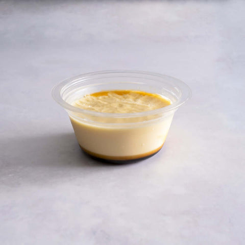 Caramel Flan served in a plastic bowl on marble, front view.