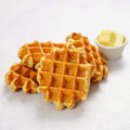 Assortment of Liege Waffles arranged on marble, with a small jar filled with butter, front view. 