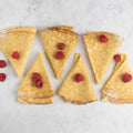 6 crèpes from At Home French Bakery with some raspberries next to it, set on marble, seen from above.