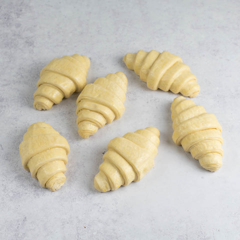 6 unbaked croissants on marble, front view.