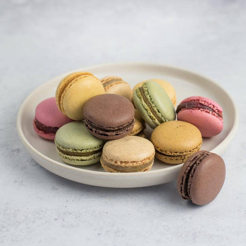 Assortments of 12 Classic French Macarons arranged in a round plate placed on marble, front view.