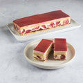 A large Strawberry Strip Cake placed in a tray and two small pieces of Strawberry Strip Cake placed in a round plate, seen from the front. 