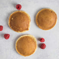 3 Strawberry-Filled Pancake placed on a marble with some raspberries next to it, seen from above. 