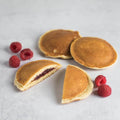 Strawberry-Filled Pancake, one cut in half with some raspberries next to it, placed on a marble, front view.