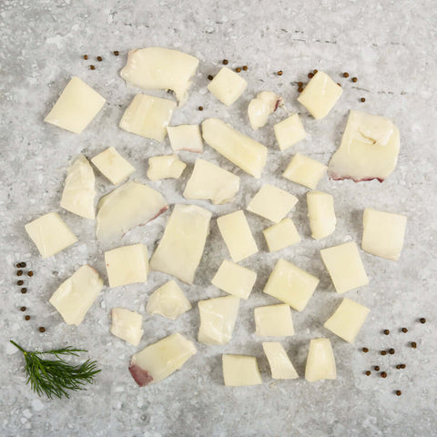 Assortment of Cuttlefish Cubes laid out on marble, with some dill leaves and black peppercorns next to it, seen from above.