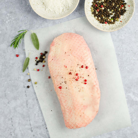 Moulard Magret Duck Breast placed skin side down on a sheet of baking paper, on marble with some pink and black peppercorn, seen from above. 