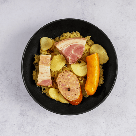 Choucroute Garnie Alsacienne (Alsatian Sauerkraut) cooked in a round plate, placed on marble, top view.