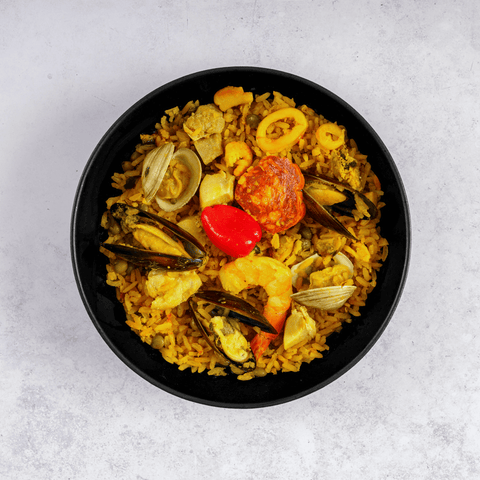 Paella Valenciana in a round dish, placed on marble, top view.