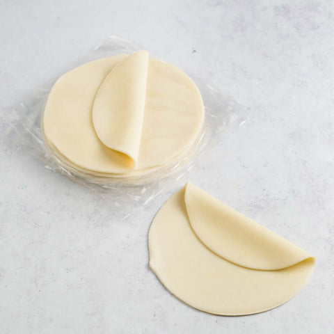 Empanada Dough stacked in a plastic package, with an Empanada Dough taken out, placed on marble, seen from above.